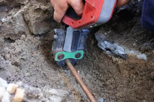 Hands of a plumber fixing an underground hot water pipe leaking with a tool. 