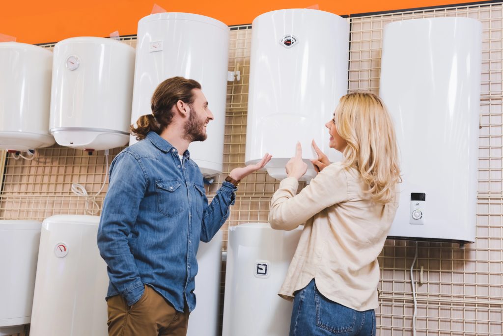 Smiling boyfriend pointing with hand and girlfriend pointing at boilers in the appliance store