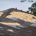 Wind damaged house roof with missing asphalt shingles after hurricane