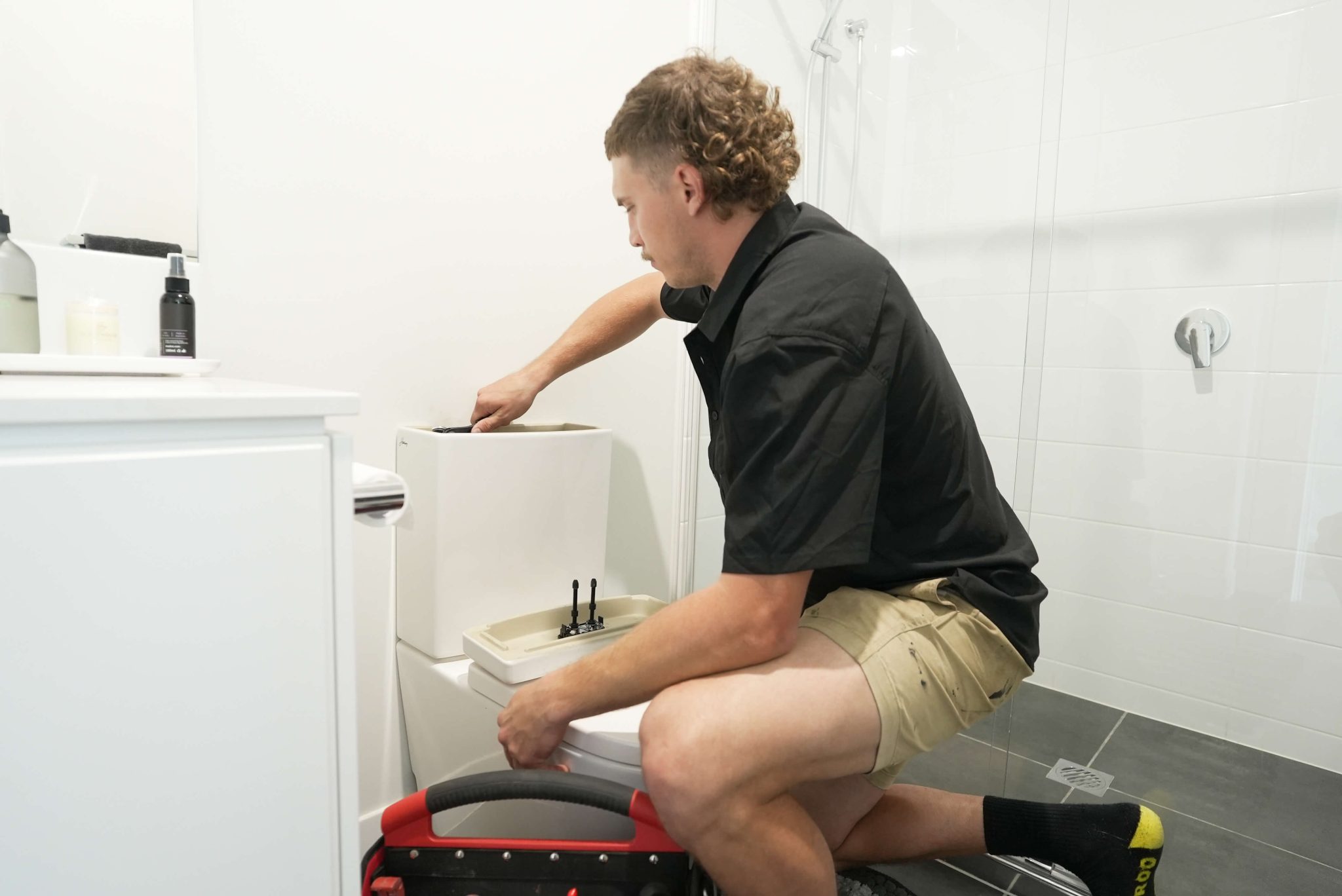Bathroom plumbing Brisbane technician repairing toilet cistern in modern home bathroom.