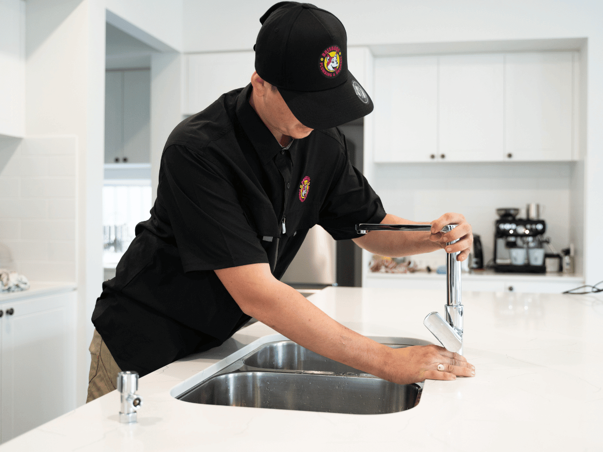 Plumber performing kitchen plumbing services Brisbane, installing modern mixer tap on sink.